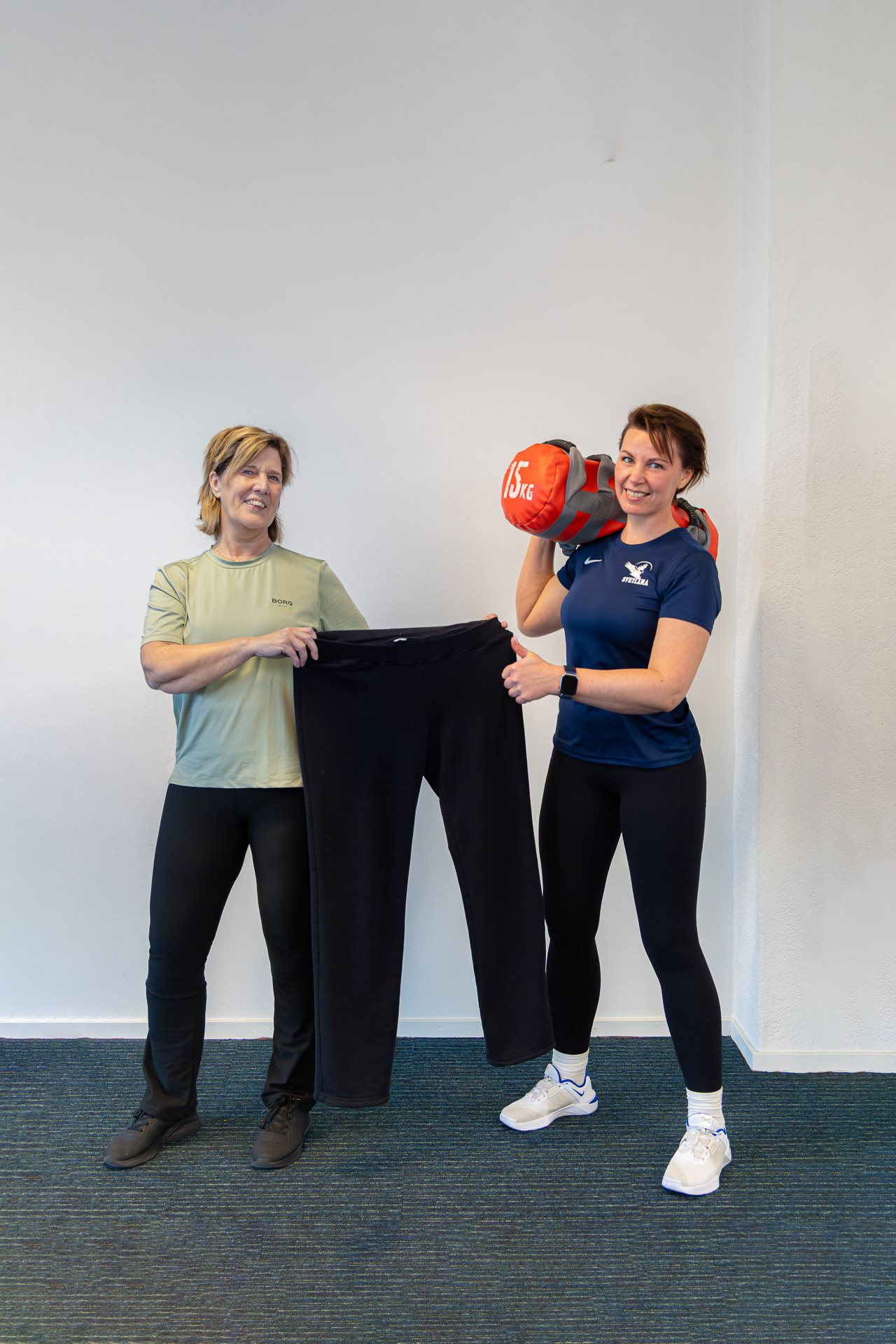 Bea met haar oude broek na 15 kilo afvallen, naast haar trainer