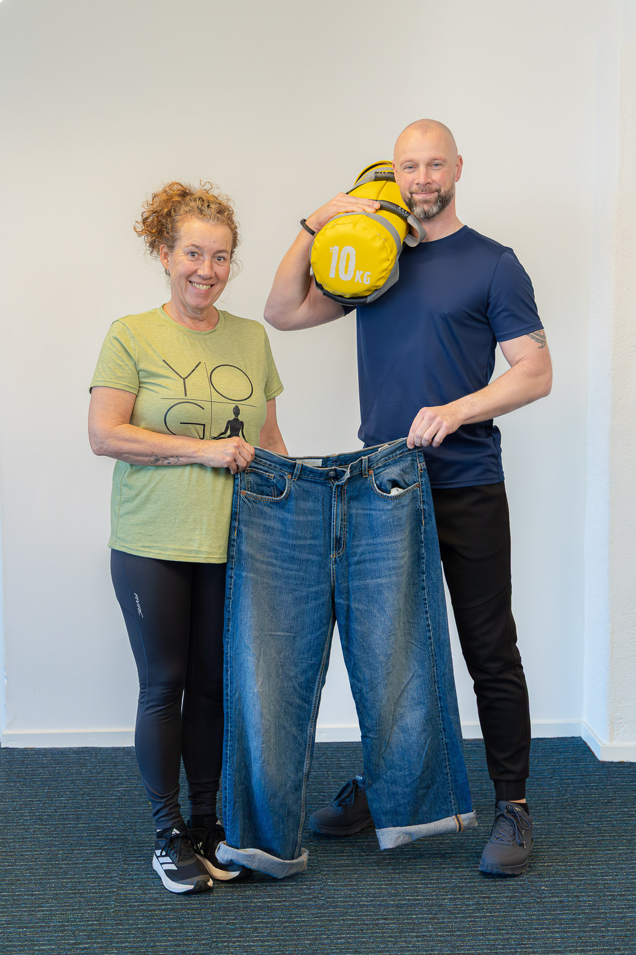 Stefanie met haar oude spijkerbroek na 10 kilo afvallen, naast haar trainer